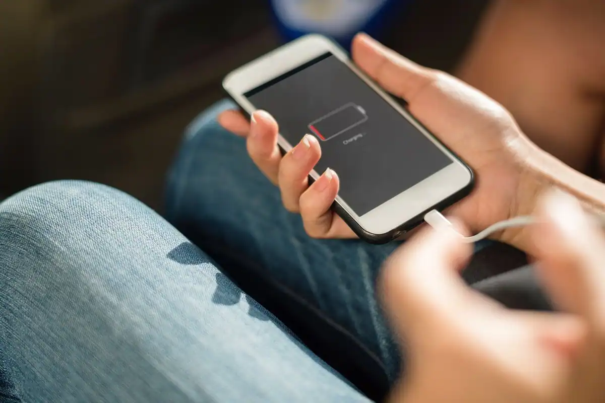Telefon conectat la cablu de încărcare, cu pictograma bateriei descărcate pe ecran