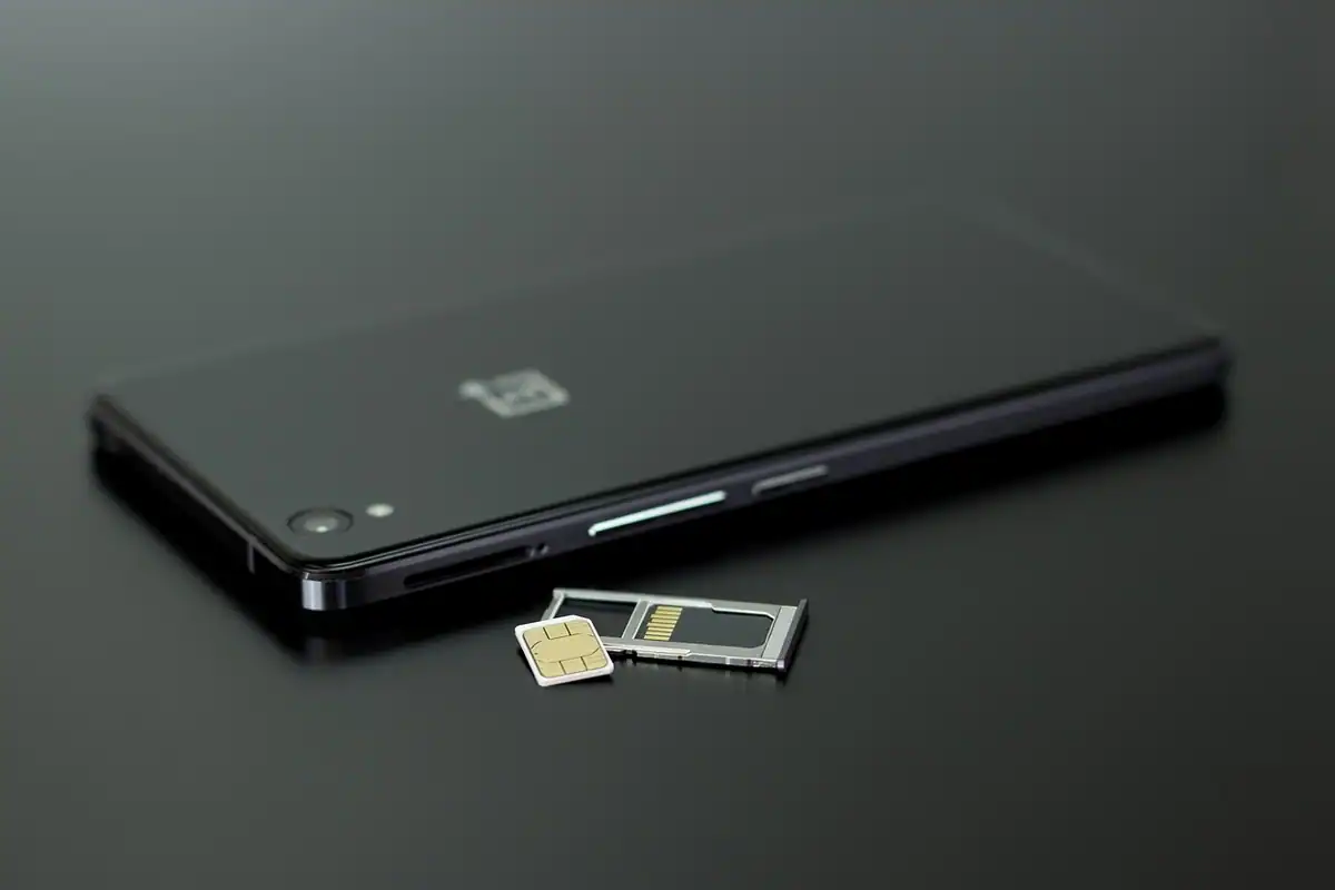 Telefon negru așezat pe masă, cu tăvița pentru cartela SIM scoasă alături