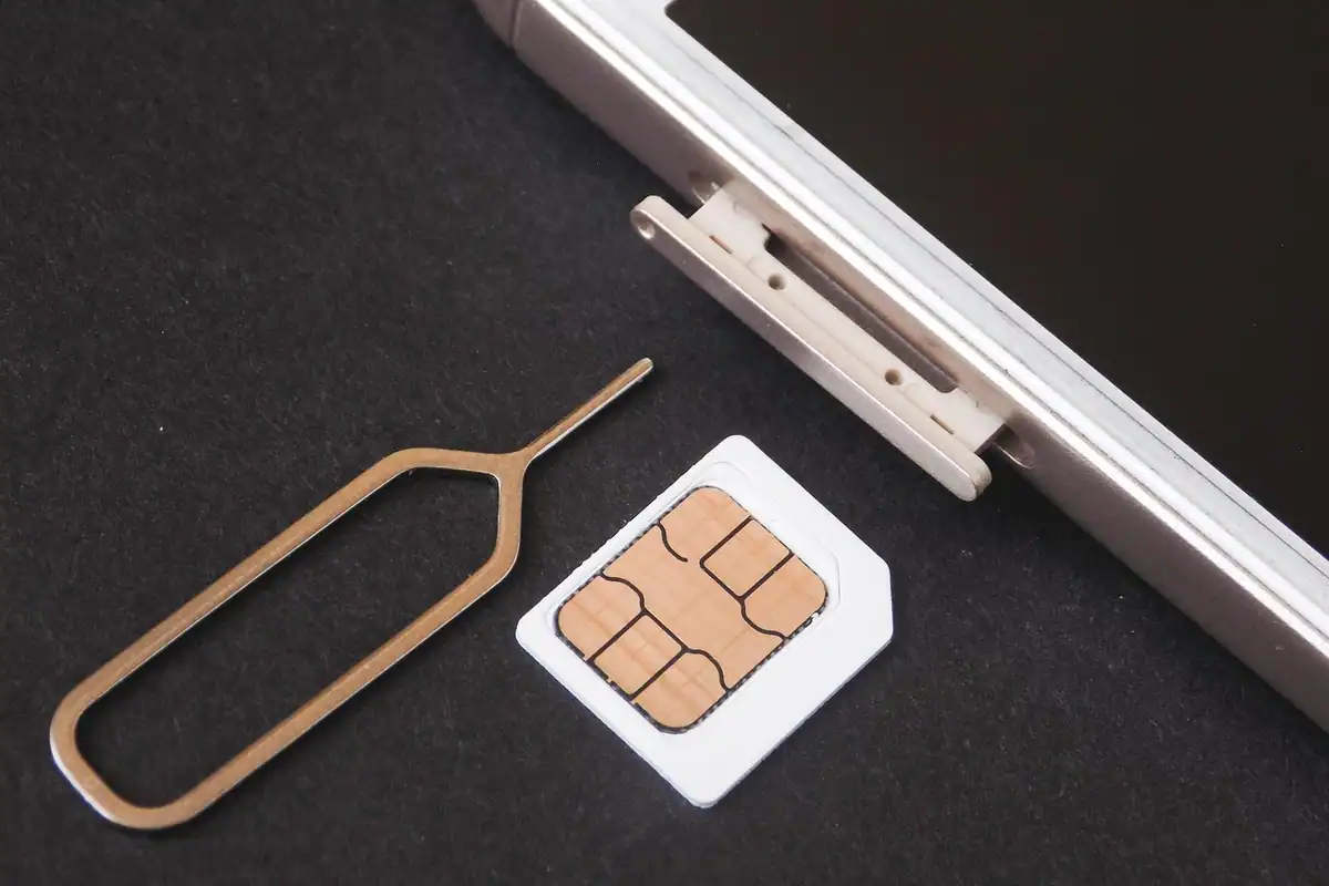 Cartelă SIM și ac de extragere lângă tăvița unui telefon