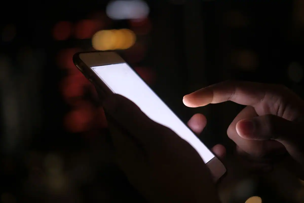 Degete care ating ecranul luminos al unui telefon nou, într-o cameră întunecată