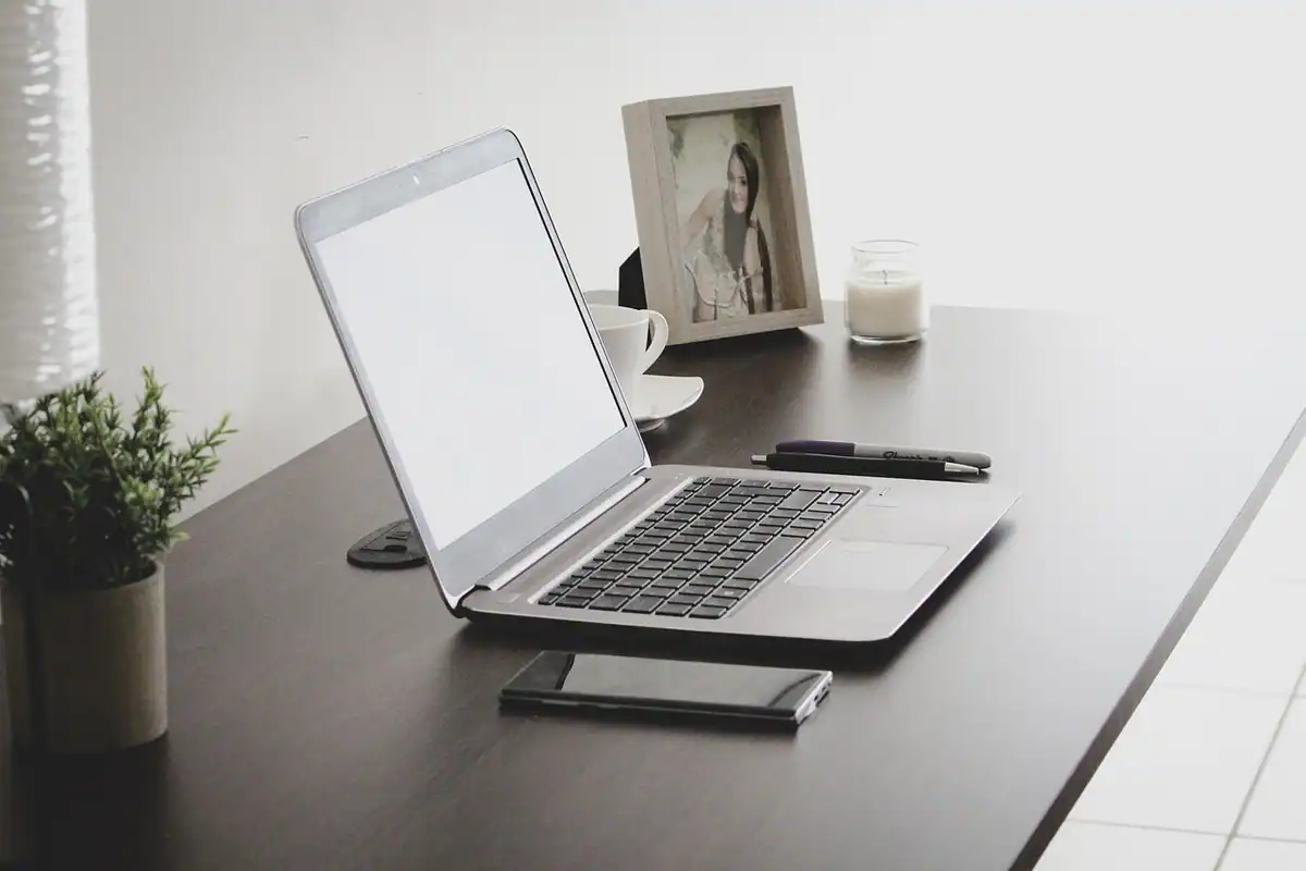 Laptop deschis pe un birou, lângă un telefon și o fotografie înrămată