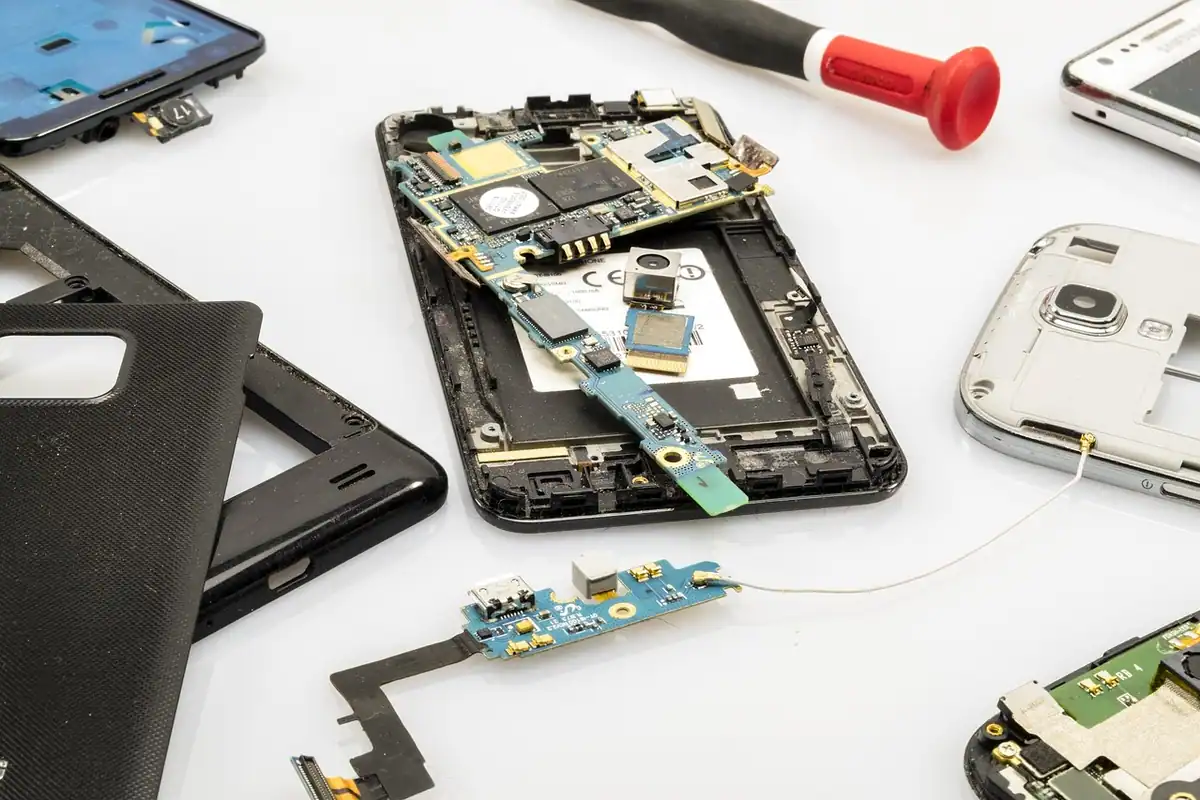 Componente electronice și șurubelnițe lângă un telefon demontat pe o masă albă