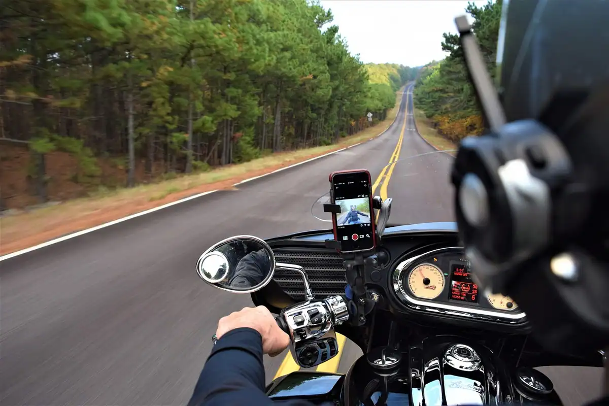 Telefon montat pe ghidonul unei motociclete, pe un drum printre pomi