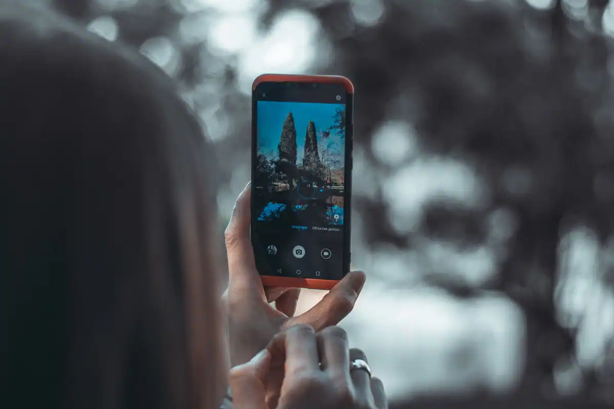 Femeie care fotografiază cu telefonul un peisaj urban printre copaci