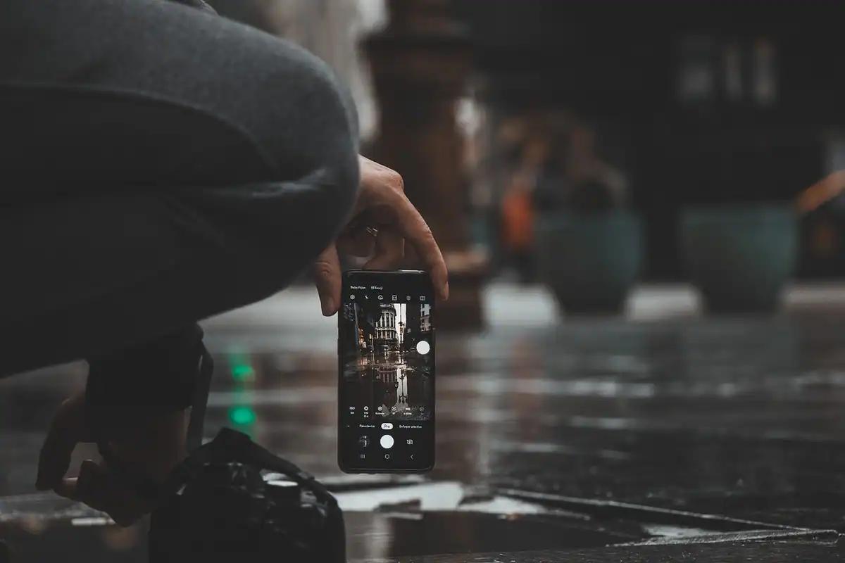 Persoană care fotografiază cu telefonul aplecată deasupra unei suprafețe ude