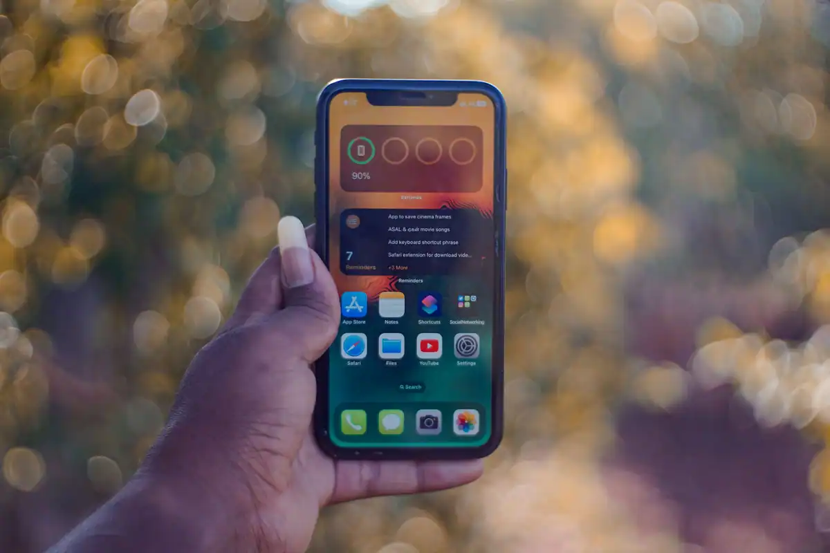 Mână ținând un telefon cu pictograme de aplicații, pe fundal cu lumini estompate
