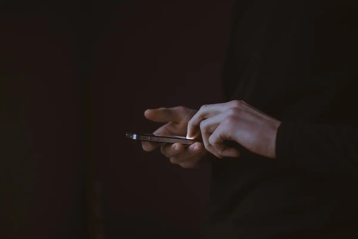 Mâini care țin un telefon în întuneric, cu ecranul stins