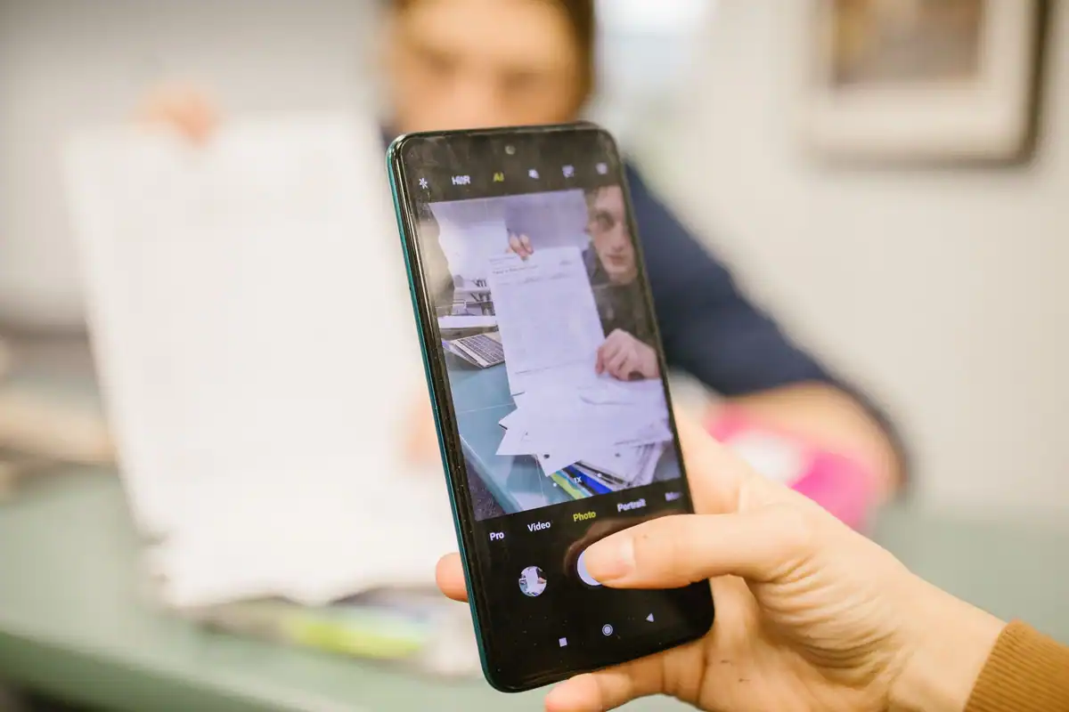 Mână care fotografiază cu telefonul o foaie de hârtie pentru a o scana