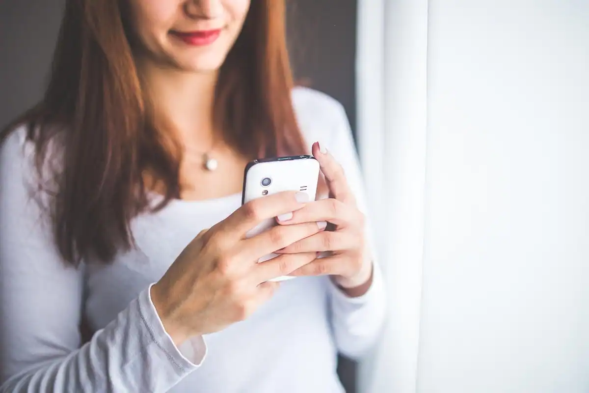 Femeie zâmbind, cu un telefon alb în mâini, într-o încăpere luminoasă