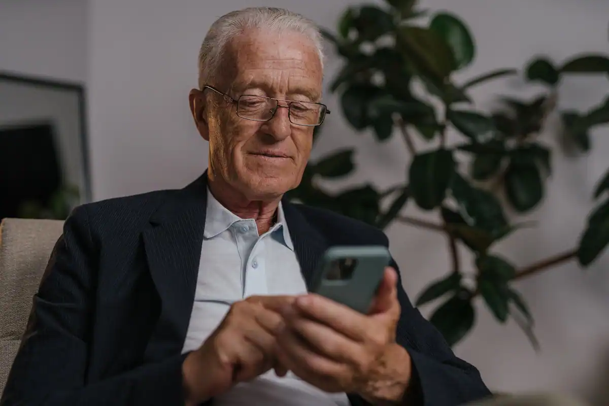 Bărbat în vârstă, cu ochelari, citind pe ecranul unui telefon