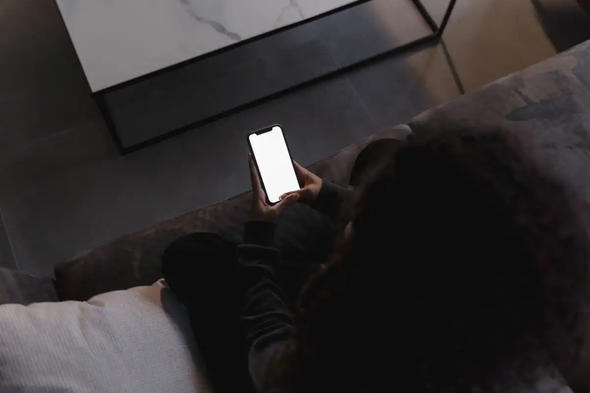 Persoană întinsă pe canapea, care folosește un telefon în lumină slabă