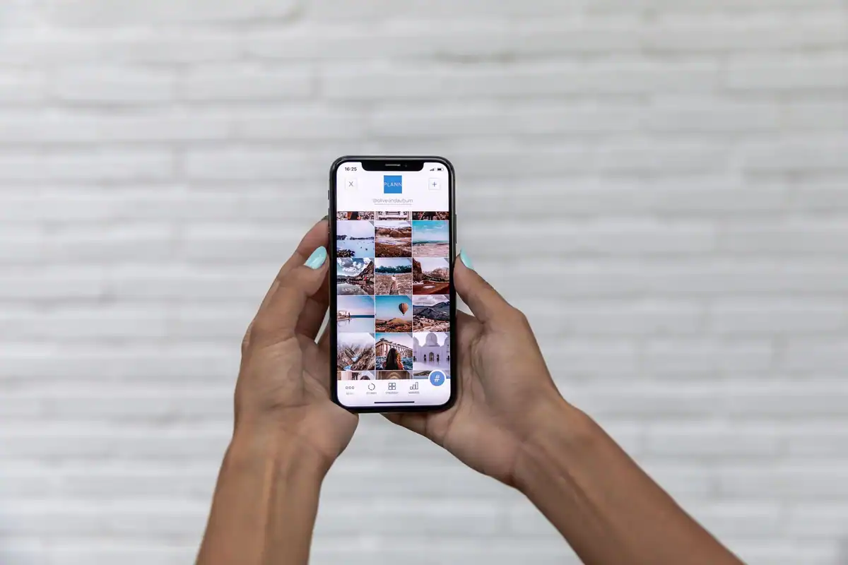Mâini care țin un telefon cu galeria de fotografii deschisă, pe fundal alb