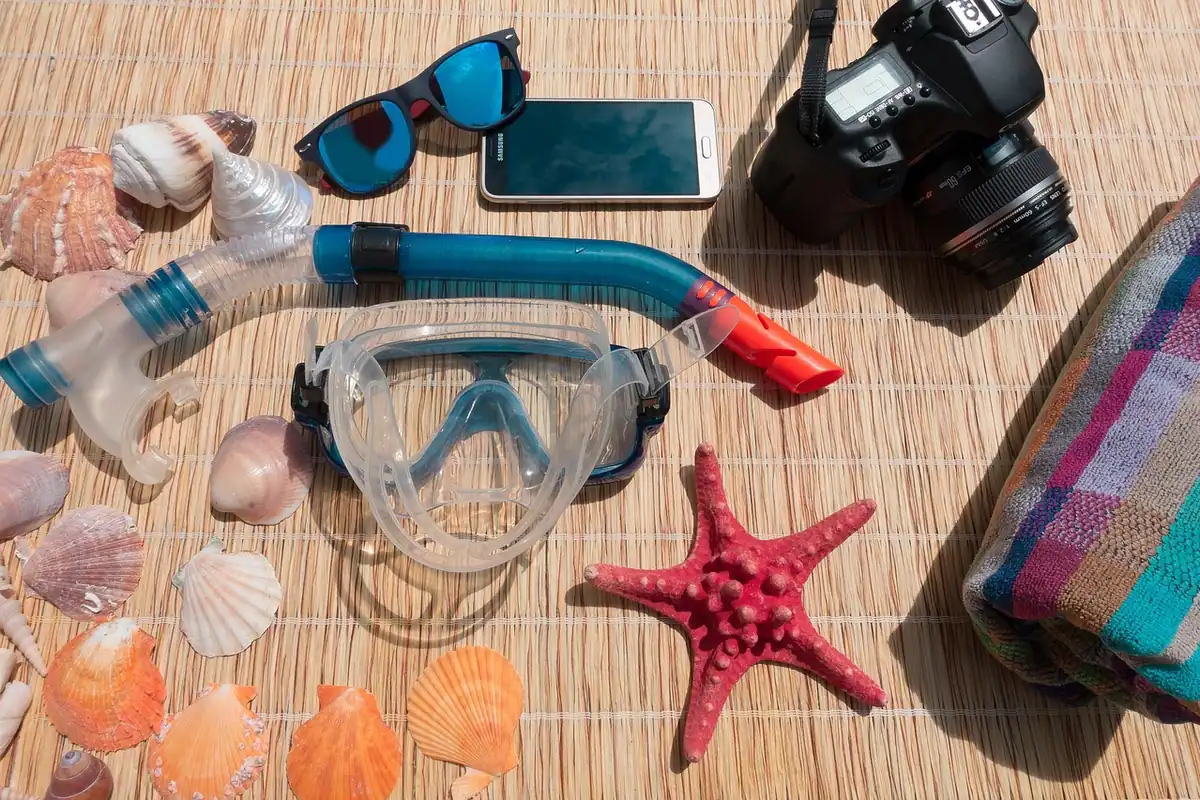 Telefon și aparat foto printre scoici, ochelari de înot și un snorkel