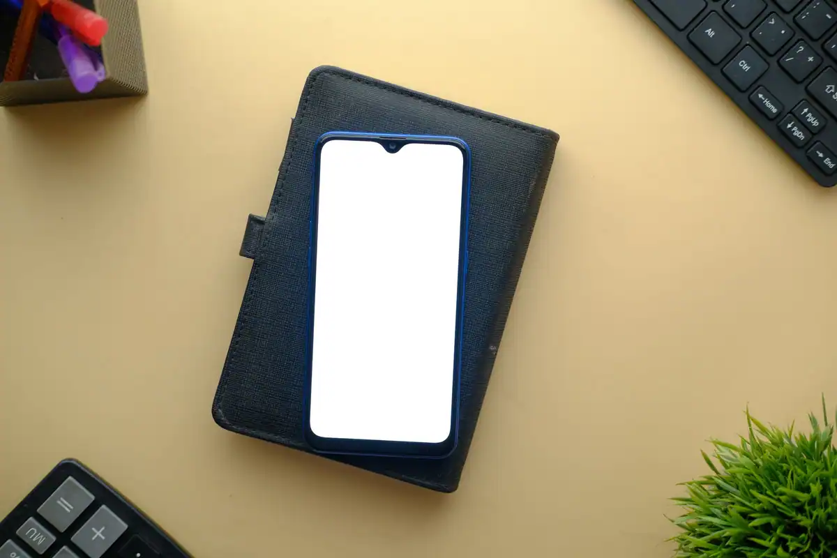 Telefon cu ecranul alb pe o husă-portofel, pe un birou cu tastatură