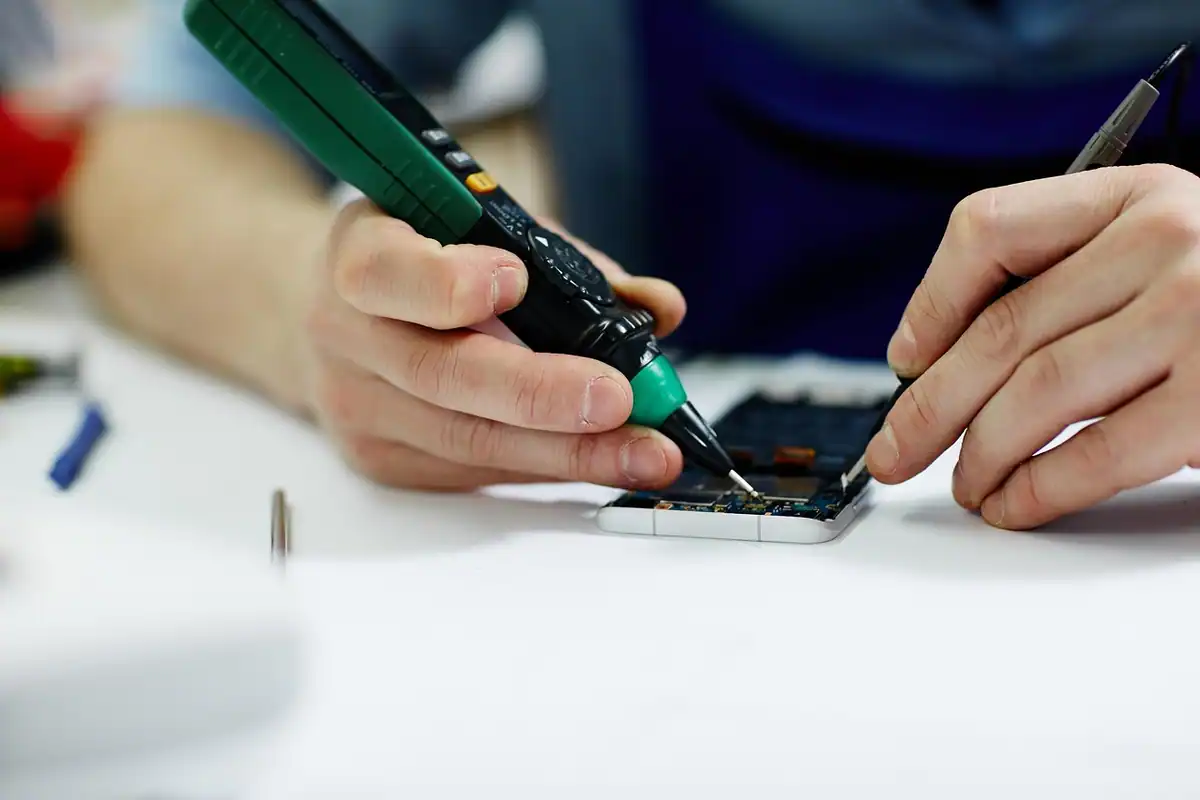 Mână care repară cu o șurubelniță electrică placa unui telefon