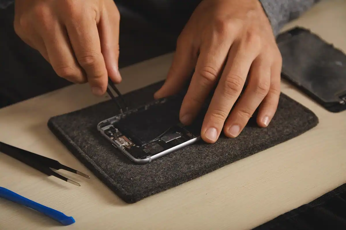 Mâini care inspectează cu penseta interiorul unui telefon pe un suport textil