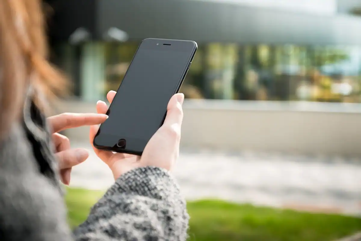Femeie care atinge ecranul unui telefon negru, pe fundal verde estompat