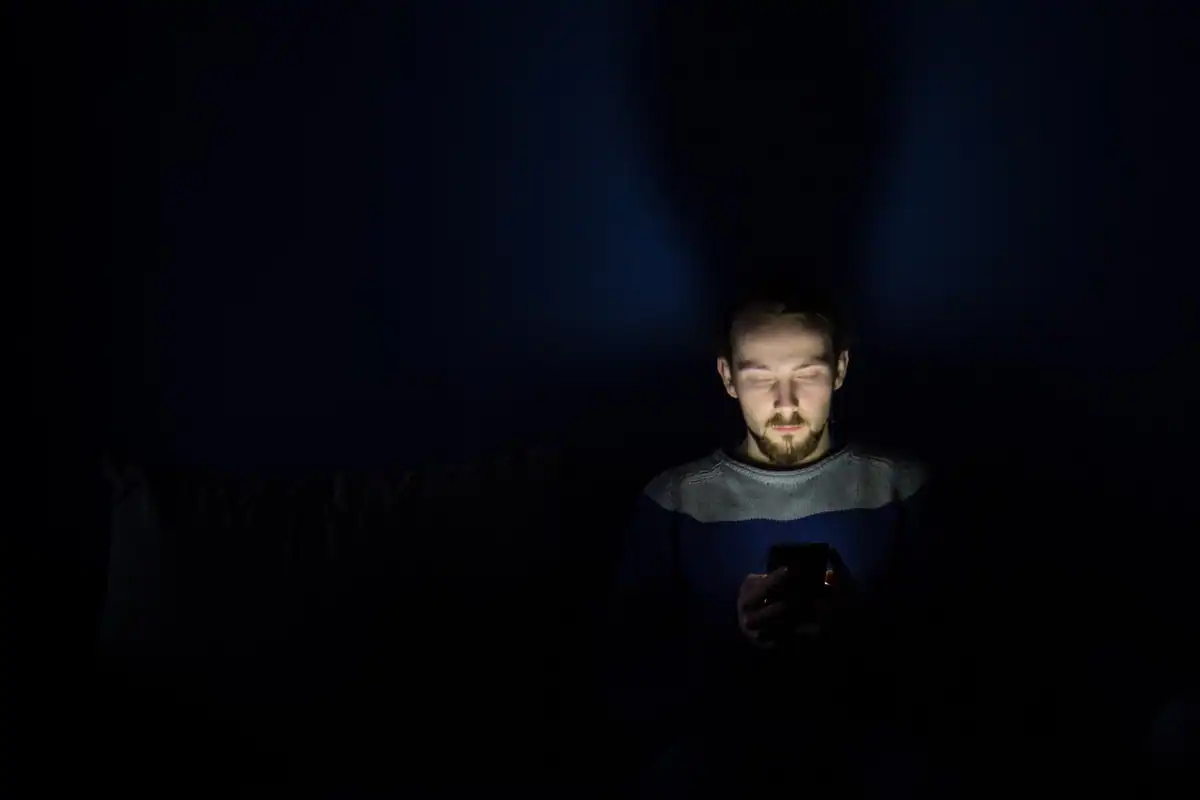 Bărbat în întuneric, cu fața luminată de ecranul telefonului