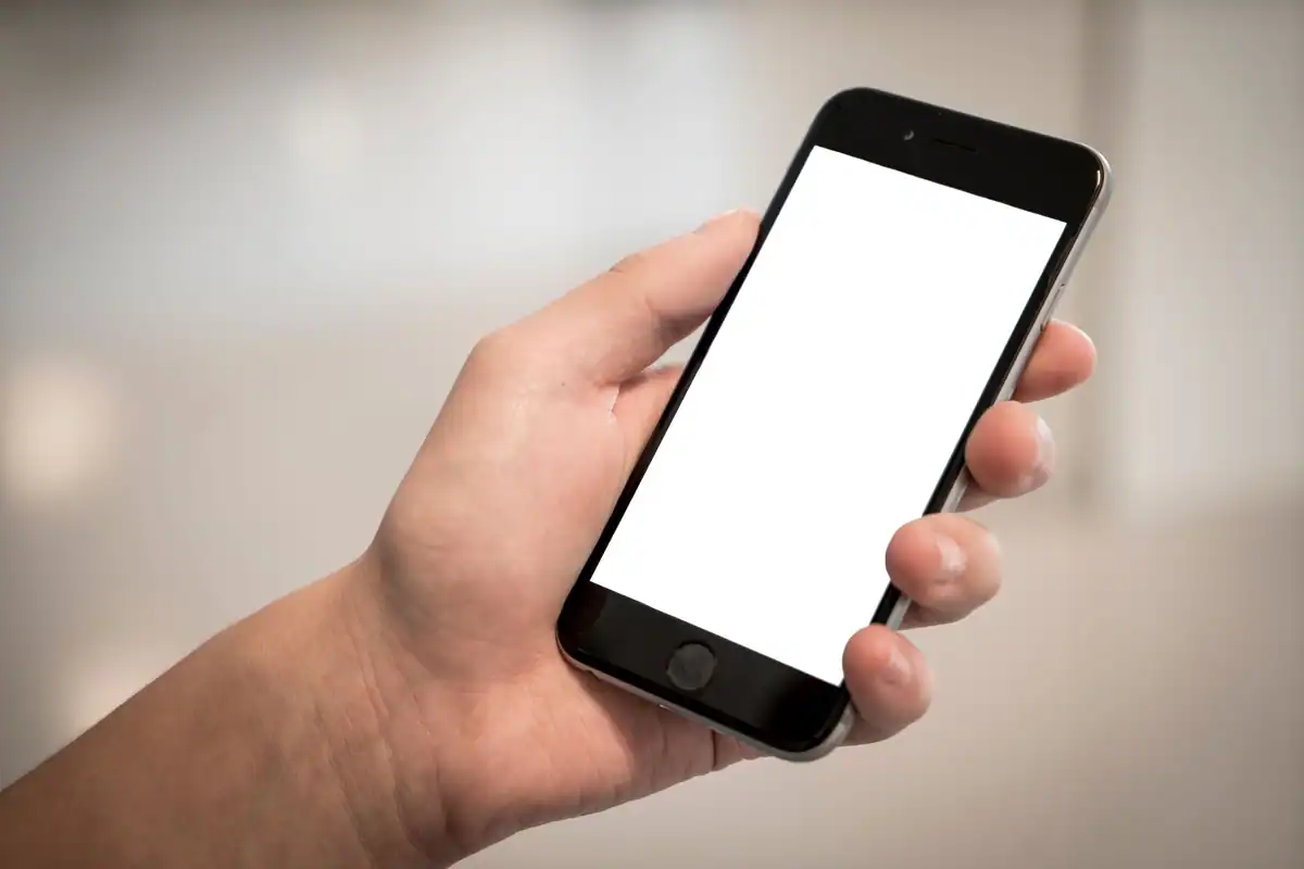 Mână care ține un telefon cu ecran alb, într-o încăpere luminoasă
