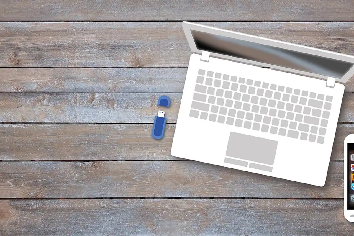 Laptop alb cu un stick USB albastru pe o masă din scânduri